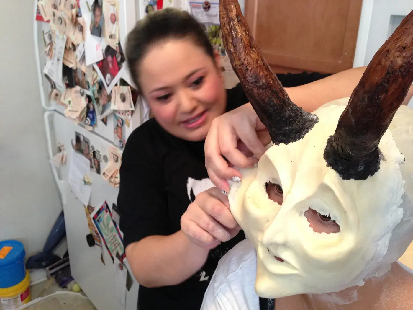 Tommy fitting a pale horned facial prosthetic to a seated person