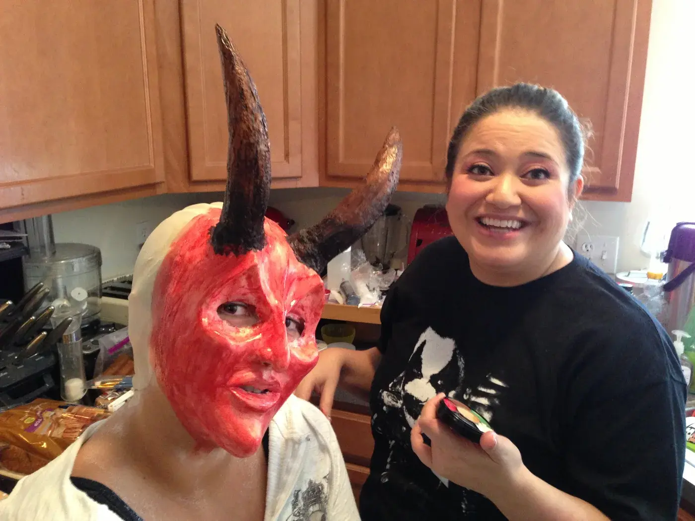 Tommy holding a brush beside a person wearing a red horned facial prosthetic